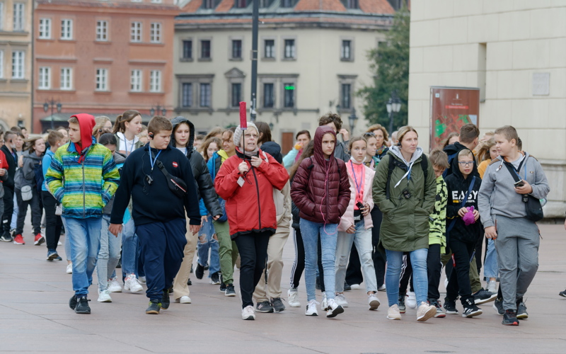 24 - Group of children and supervisors walking through a city square